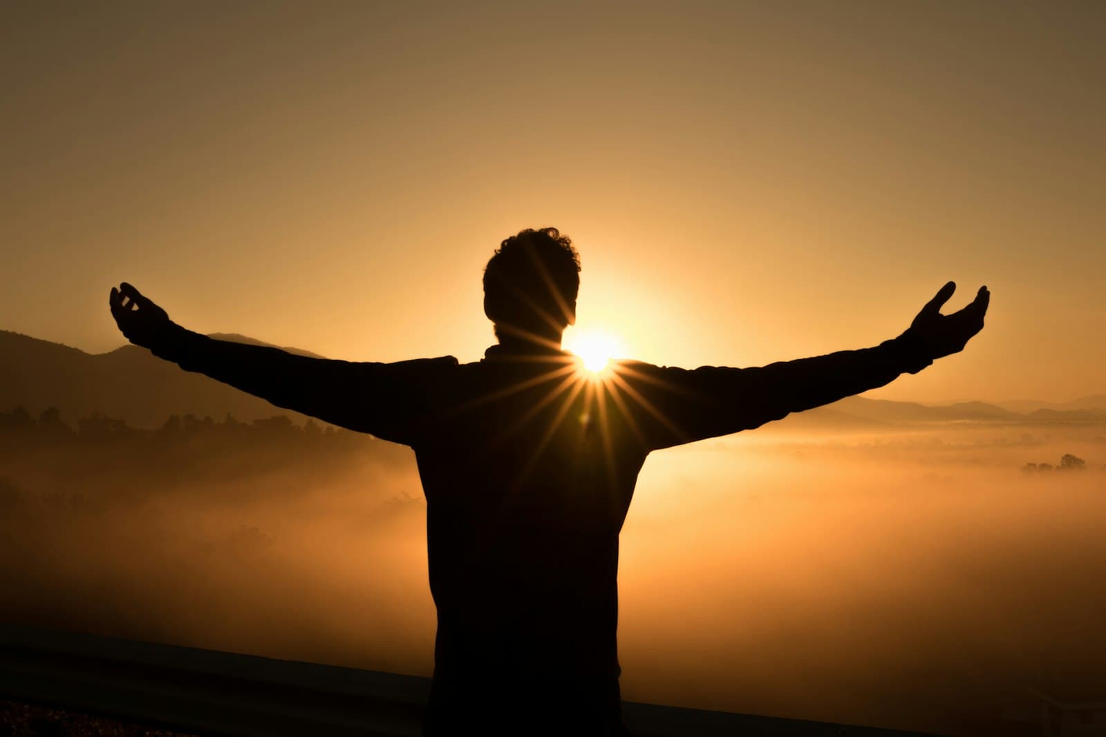 Silhouette of a person with arms raised at sunrise over a foggy valley, representing a personal goal reached