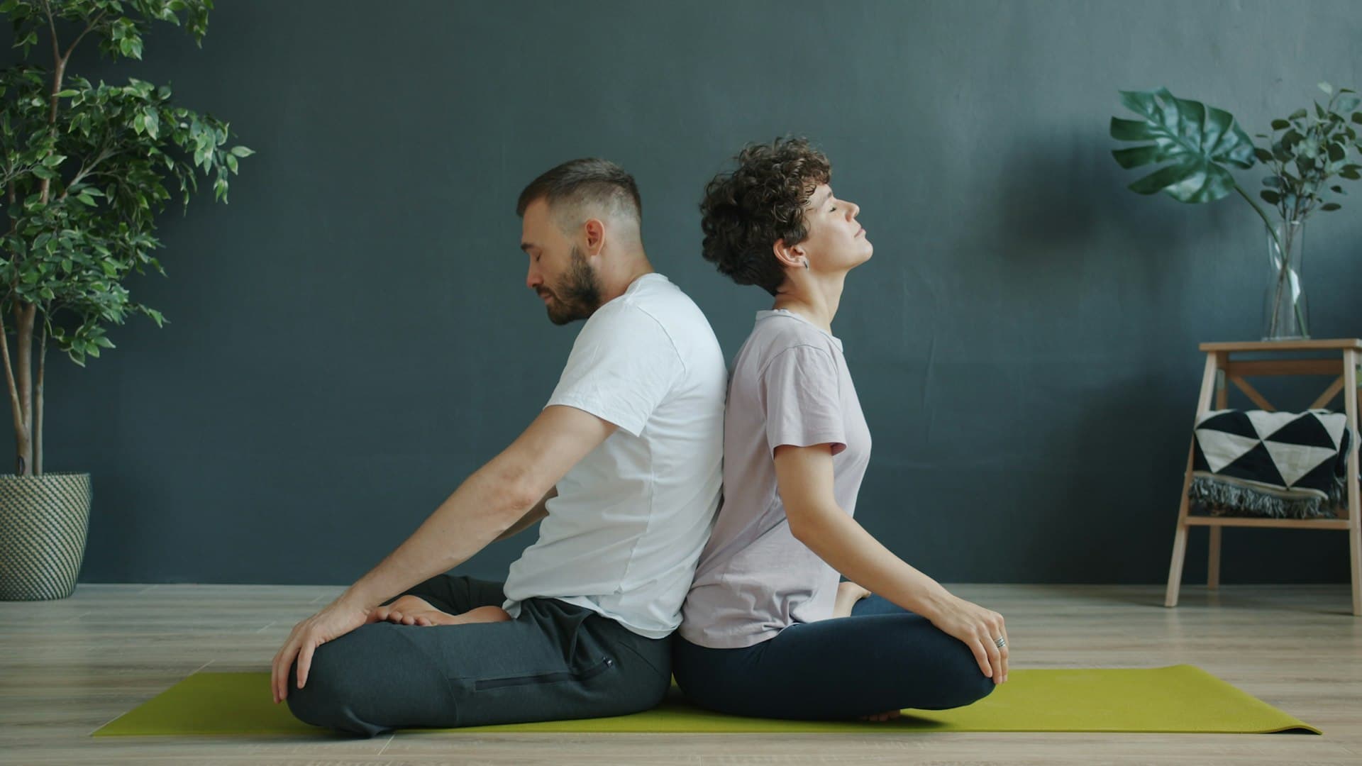 A man and woman sitting back to back on a yoga mat, stretching and breathing mindfully together